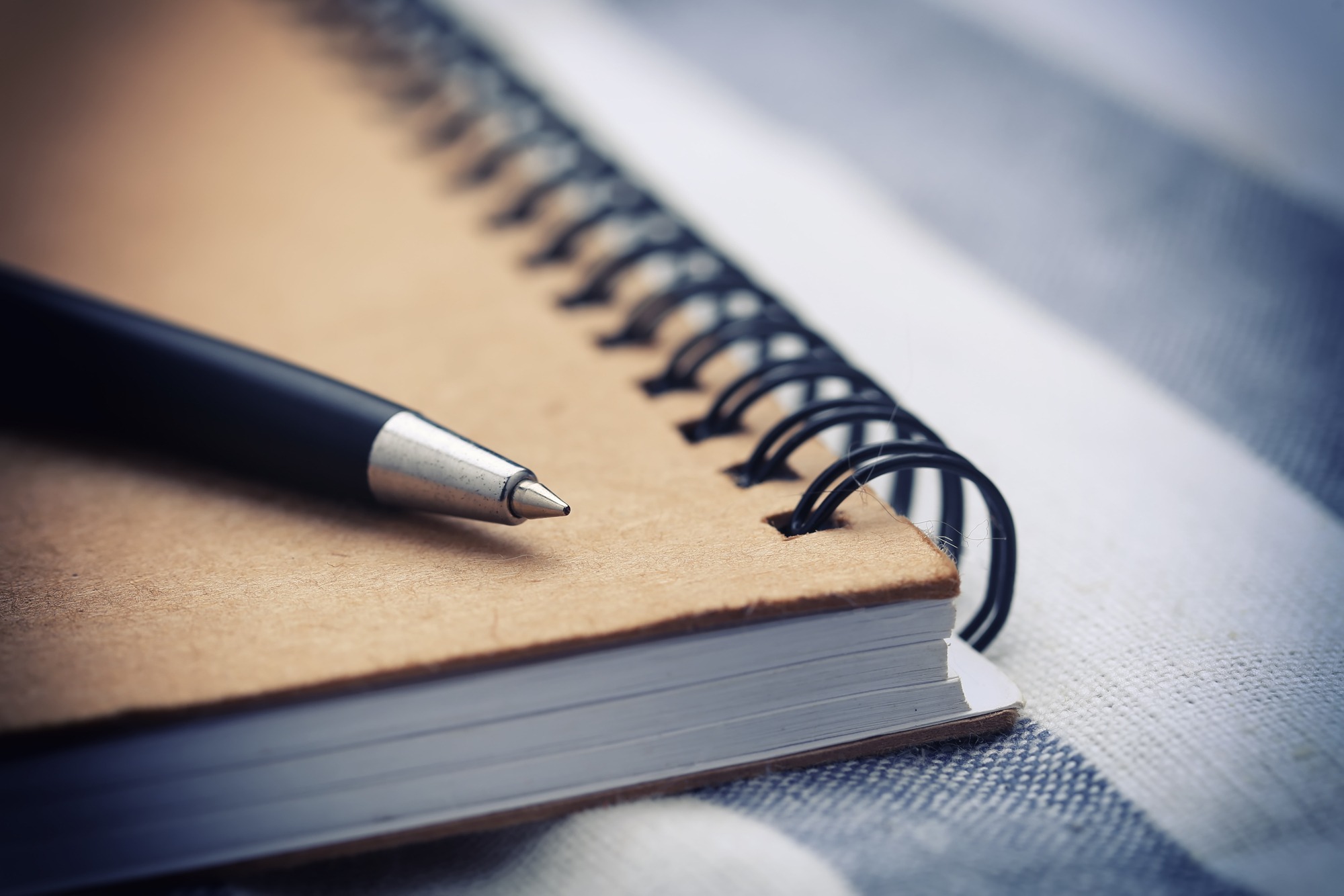 Black pen rests on the edge of a spiral-bound notebook, showcasing a simple writing setup on a textured surface.